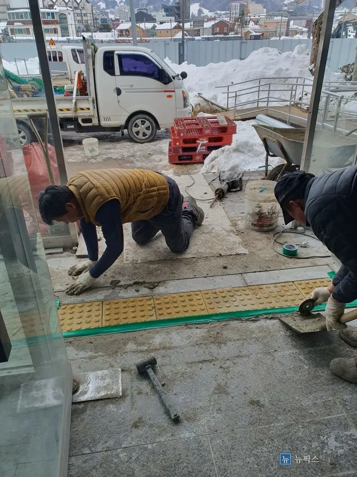 파낸 자리에 몰탈을 깔고 노란 점자블럭을 앉히는 두 작업자