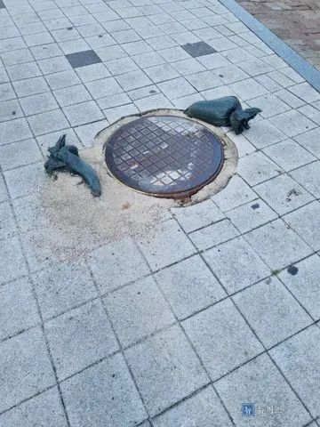 모래주머니로 눌러둔 보도블럭 위 낡은 정화조 맨홀뚜껑