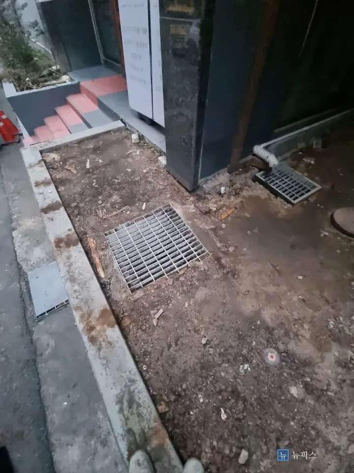 평탄하지 않은 흙바닥과 배수 그레이팅이 보이는 작업 전 샛길